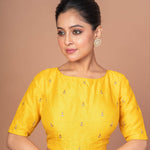 An Indian Woman Dressed in a Yellow Raw Silk Blouse with Boat Neckline and Gold Floral Work: Anvi Couture - Image 2