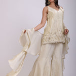 A woman modeling a cream-colored traditional outfit with a flowing skirt and embroidered sleeve, set against a plain light background.