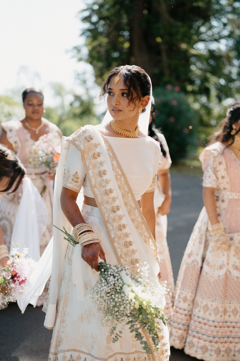 Woman in a traditional outfit with floral decorations, walking outdoors with greenery in the background.