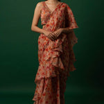 Woman wearing vibrant orange organza saree with scattered floral print and hand-embroidered matching stitched blouse, styled for party wear