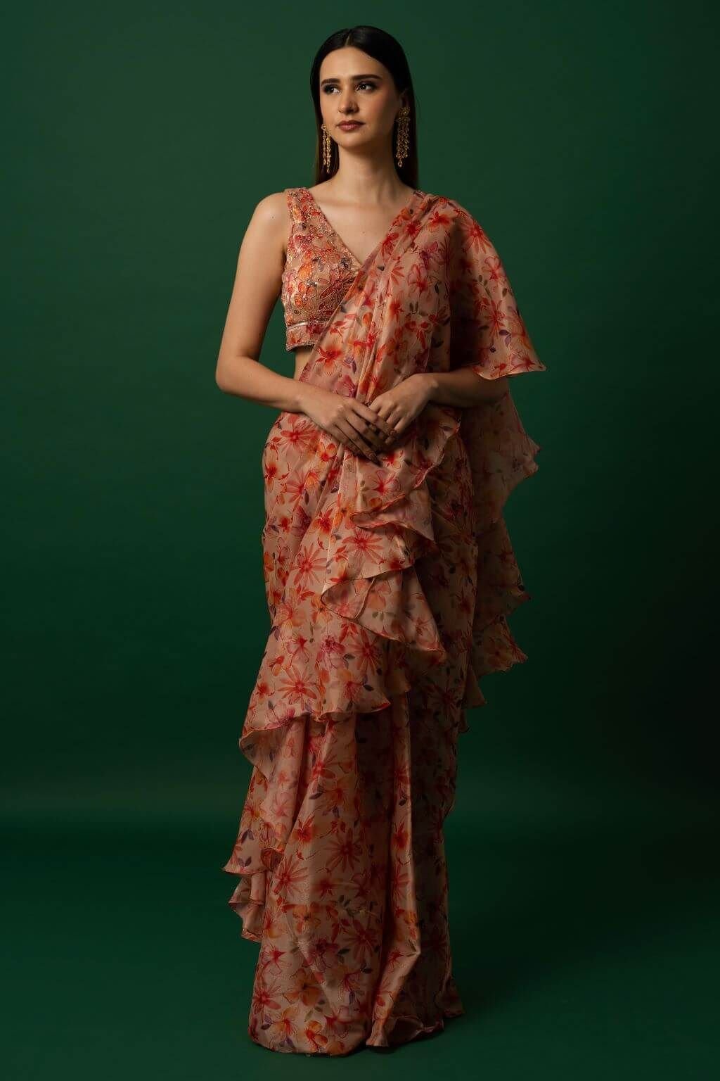 Woman wearing vibrant orange organza saree with scattered floral print and hand-embroidered matching stitched blouse, styled for party wear