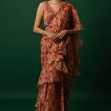 Woman wearing vibrant orange organza saree with scattered floral print and hand-embroidered matching stitched blouse, styled for party wear